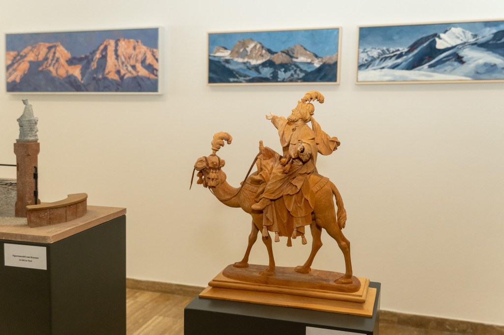 Schnitzerer von Josef Zeisler vor Bergbildern von Veronika Kolp